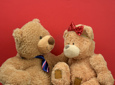 两只棕褐色的泰迪熊坐在对面红色背景爱情和约会概念图片