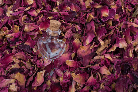 以干玫瑰花瓣背景的心形瓶子高清图片