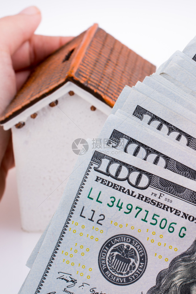 人类手拿着一栋模范房子站在白底的美元钞票旁边图片