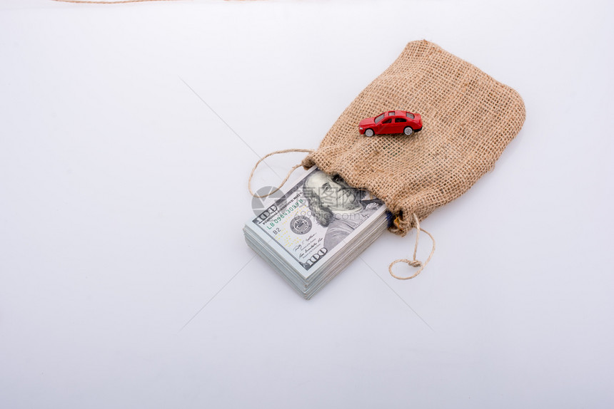 一辆白色背景的玩具汽车和一袋的美元包裹图片