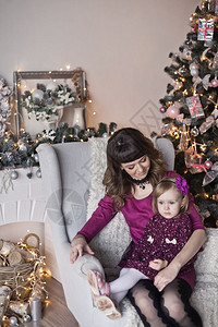 婴儿和母亲坐在圣诞树附近的椅子上女儿和母亲坐在圣诞树附近的椅子上背景图片