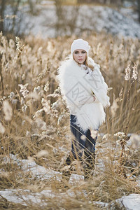 穿着白色毛皮大衣的女孩站在冬季中草丛间图片