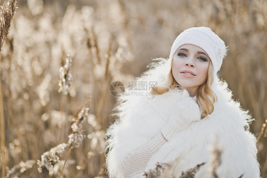 穿着白色毛皮大衣的女孩站在冬季中草丛方图片