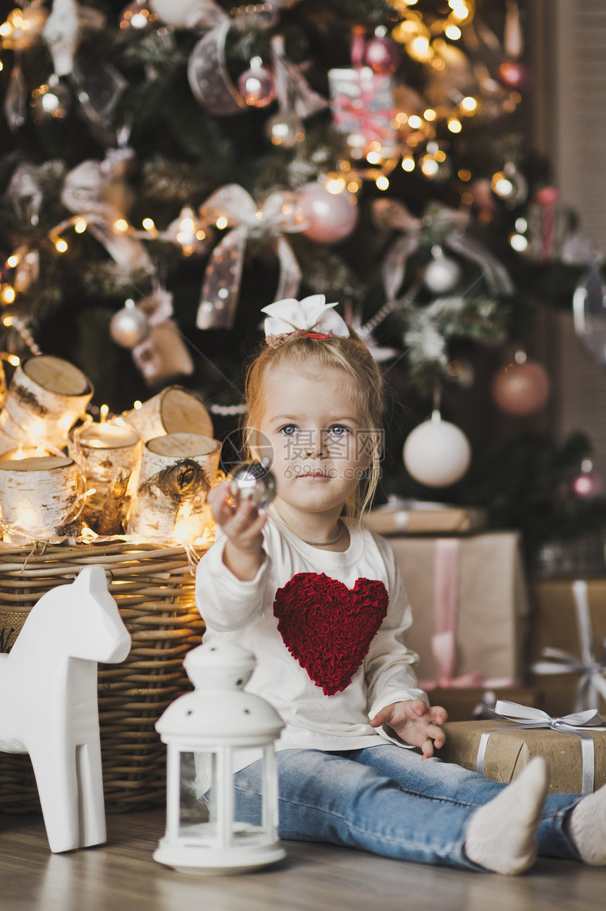 坐在圣诞树旁边的地板上一个小女孩坐在圣诞树下面带礼物7239图片