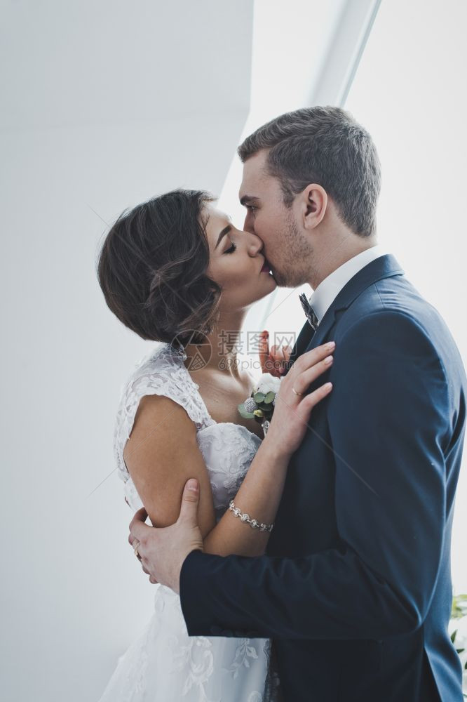年轻夫妻在窗口的明亮背景上温柔地亲吻对方在明亮的Windows6459的背景下新婚夫妇温柔地亲吻新婚夫妇图片