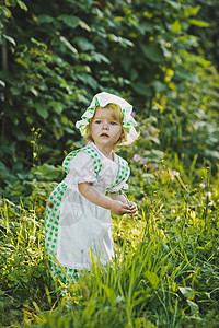 穿着绿色和白衣服的小女孩在花园里走动背景图片