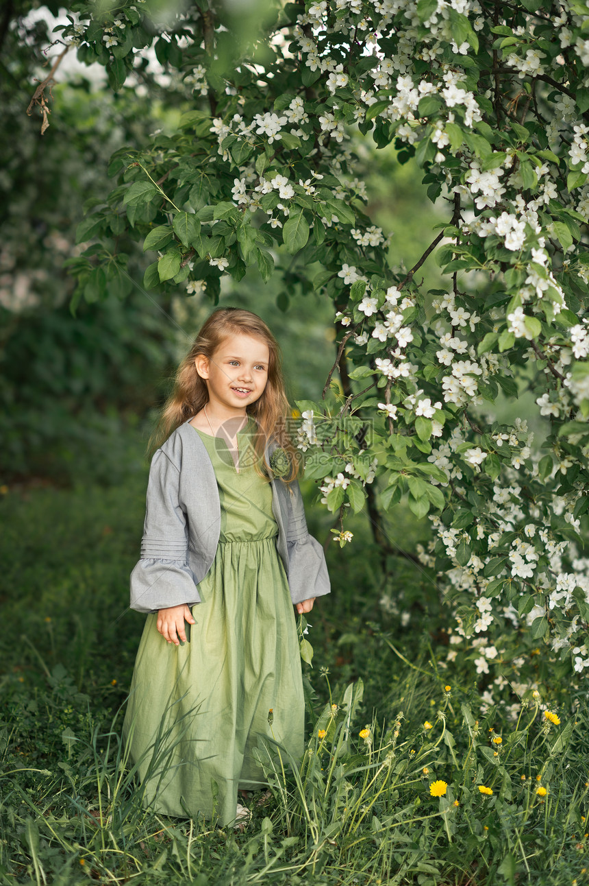 春中一个小女孩的肖像在开花树上这个孩子站在一鲜花的樱桃布希1802旁边图片