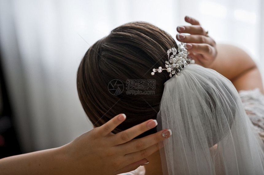 新娘调整其头发上的婚纱和珍珠首饰图片