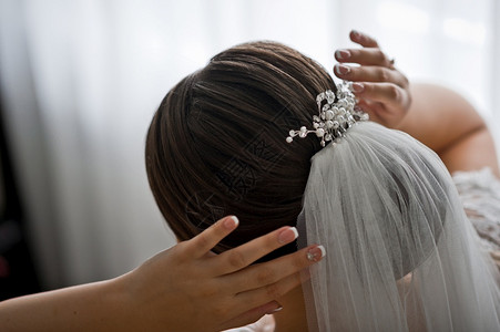 新娘调整其头发上的婚纱和珍珠首饰图片