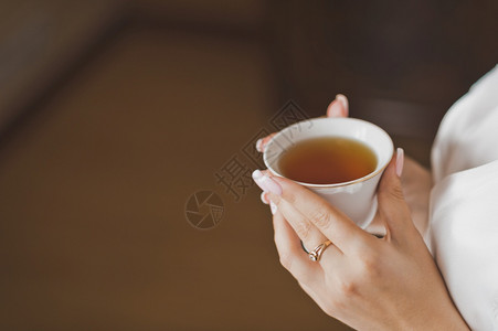 一杯茶在女孩的手中穿着晨礼服的一小杯茶在215年早晨一个美丽的女孩手中背景图片
