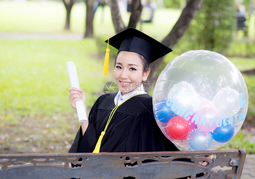 喜悦的年轻女毕业生穿着学术服和平方帽在召集仪式后气球上用COGRATSGRAD的文字引用图片