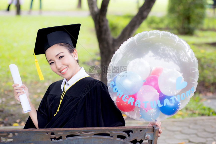喜悦的年轻女毕业生穿着学术服和平方帽在召集仪式后气球上用COGRATSGRAD的文字引用图片