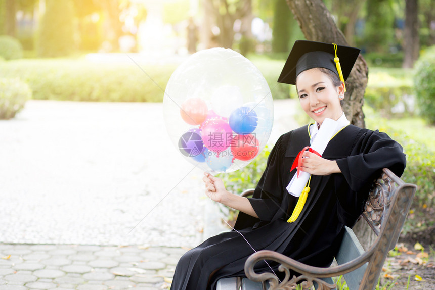 喜悦的年轻女毕业生穿着学术服和平方帽在召集仪式后气球上用COGRATSGRAD的文字引用图片