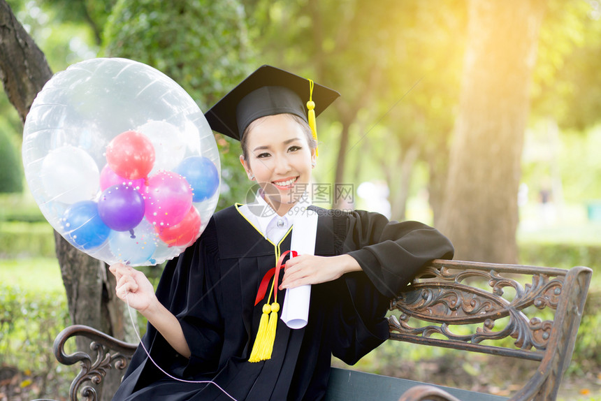 喜悦的年轻女毕业生穿着学术服和平方帽在召集仪式后气球上用COGRATSGRAD的文字引用图片