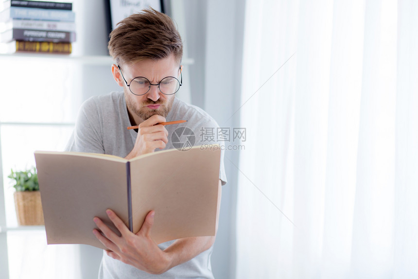戴眼镜的帅哥正在读书准备考试和思站在起居室教育概念图片