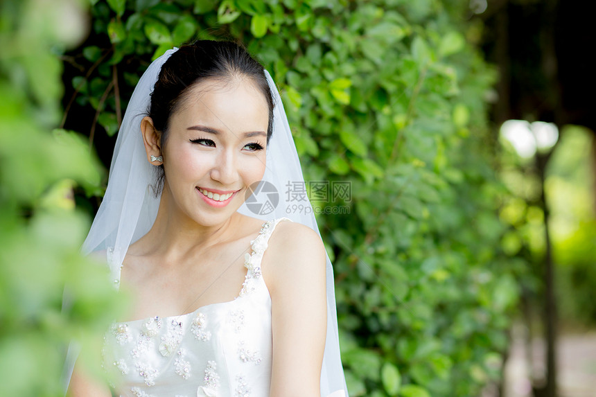 在婚礼当天美丽的年轻女子穿着白色衣服在树墙上公园中的女肖像有选择的焦点图片