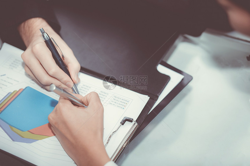 商业伙伴的密切接触将载有男女在会议室用笔手的图表和文件交给了商业伙伴图片