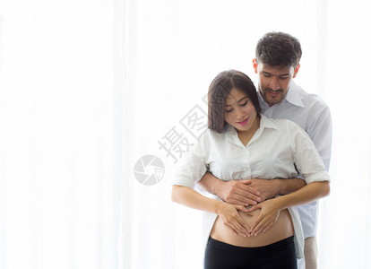 怀孕的妈和父亲站着拥抱握肚子心脏的形状用手家庭概念图片