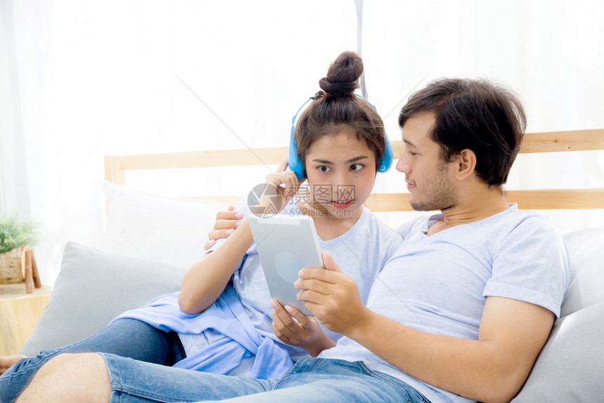 美丽的亚洲年轻夫妇听着床上有平板电脑的音乐爱约会年轻夫妇坐在床上用平板电脑坐在床上图片