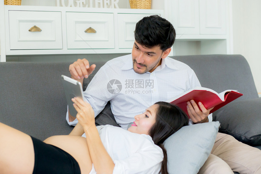 亚洲夫妇家庭年轻母亲和丈夫在家里使用平板电脑男女在沙发上躺着看平板电脑阅读书时怀孕图片