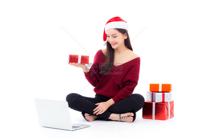年轻女穿着圣塔帽和礼物盒在圣诞节假日与网路购物同坐卧底女孩在Xma的笔记本上购物庆祝概念图片