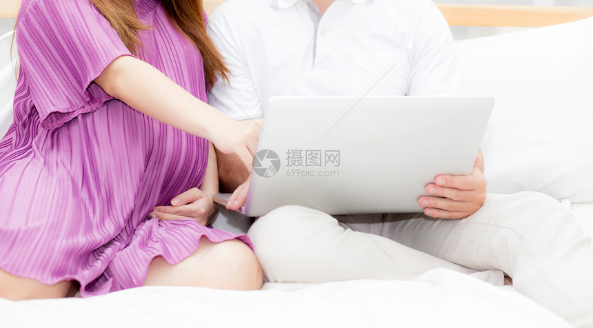美丽的怀孕家庭卧室上有笔记本电脑夫妻笔记本放松夫妻和家庭概念图片