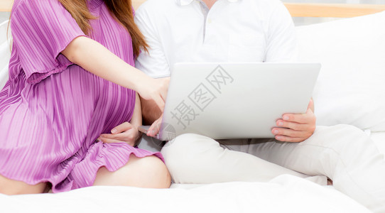 美丽的怀孕家庭卧室上有笔记本电脑夫妻笔记本放松夫妻和家庭概念图片