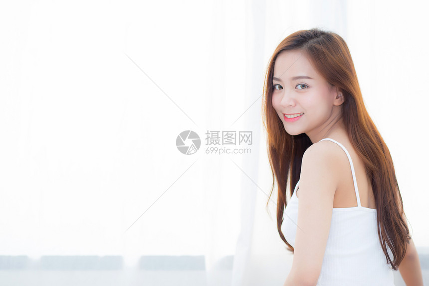 美丽的亚洲年轻女子微笑着快乐的闲暇坐在家里的床上坐在窗户旁边女孩放松健康的概念图片
