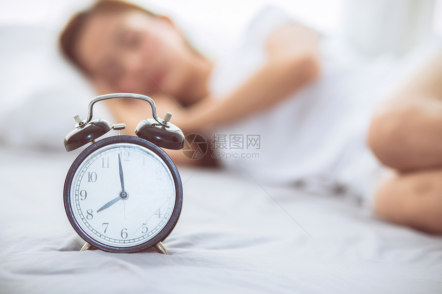 美丽的亚洲年轻女在清晨关闭闹钟醒来睡觉时图片