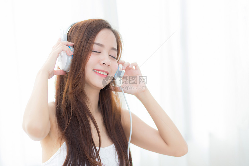 美丽的年轻女坐在卧室时享受耳机听音乐图片