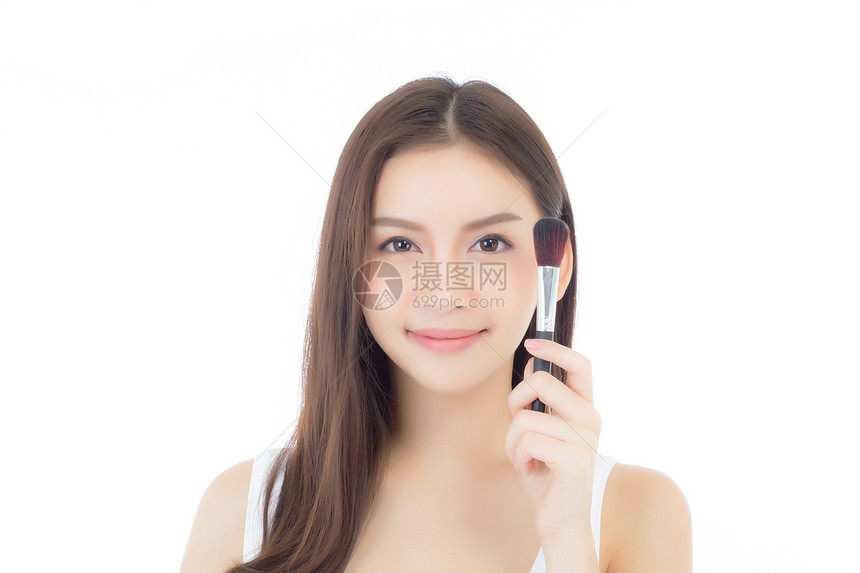 美貌的亚裔女在申请时用白色背景上孤立的脸颊刷子来弥补图片