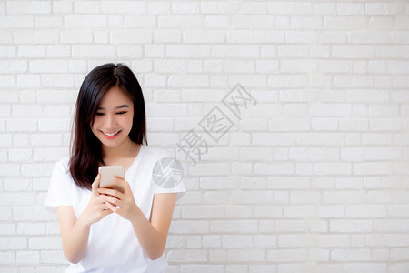 女士站在砖墙前年轻女触摸手机站在水泥砖背景上微笑自由职业女电话通信概念背景