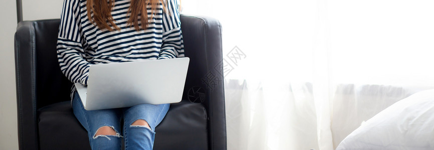 使用笔记本电脑在客厅的椅子上闲暇在网与笔记本自由职业者合作的女孩图片