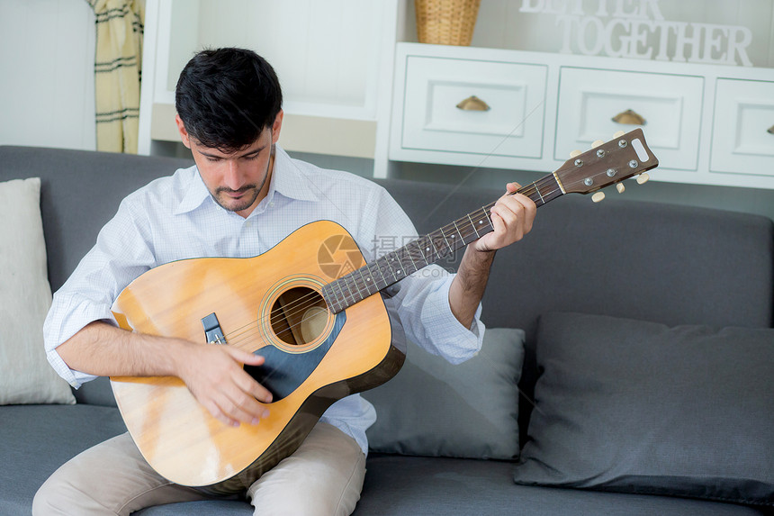 坐在沙发上玩独奏吉他音响是客厅的爱好男是吉他手图片