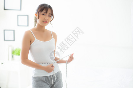 美丽的年轻女在卧室中饮食体瘦腰部大小体重较轻女孩用胶带测量健康和概念丧失了纤维素和卡路里背景图片