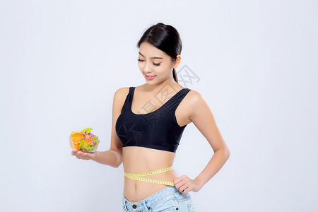 年轻美貌的女笑着拿沙拉蔬菜食物并用腰部测量体重孤立在白色背景上图片