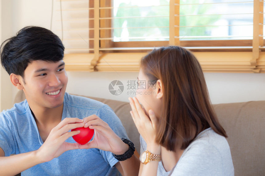 美丽的肖像年轻亚洲夫妇手势保持心型在一起丈夫给予心型妻子快乐的笑容和坐在沙发上家庭关系与爱浪漫和甜蜜的概念图片