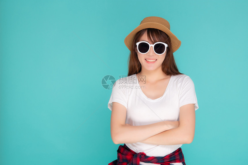 年轻女美丽肖像戴着帽子和太阳镜微笑地表达自信享受夏天的假期远离蓝色背景女孩快乐地穿着时装旅行概念图片