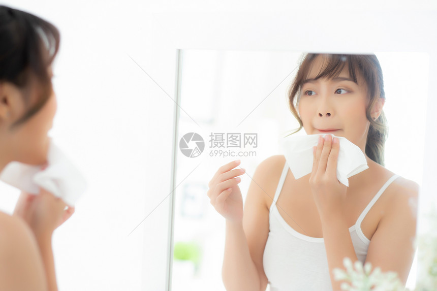 美丽的肖像年轻女微笑与皮肤护理化妆品使用油抹纸在脸上看着镜子房间的中美Asia女孩擦和清洗化妆品与组织清洁的面部概念图片