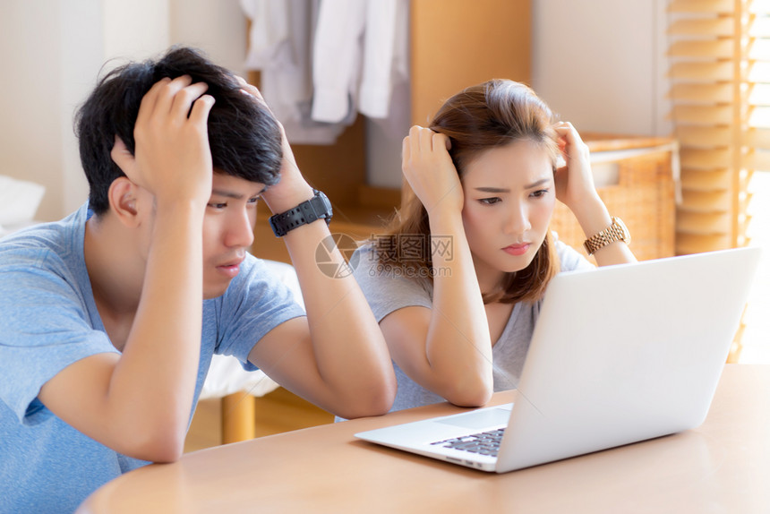 年轻一对的亚裔夫妇强调并担心问题企业的融资男女在看笔记本电脑和沮丧家庭不快乐对债务和生活方式概念的沮丧图片