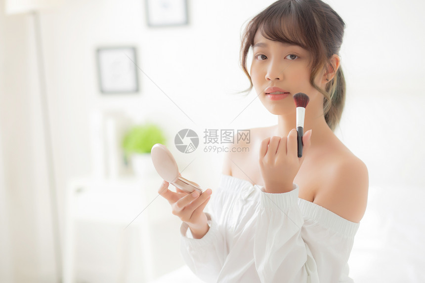 美容肖像年轻的亚洲女微笑着面部镜像化妆时在卧室里涂上刷脸的化妆品美貌女孩脸部更红皮肤护理和化妆品概念图片