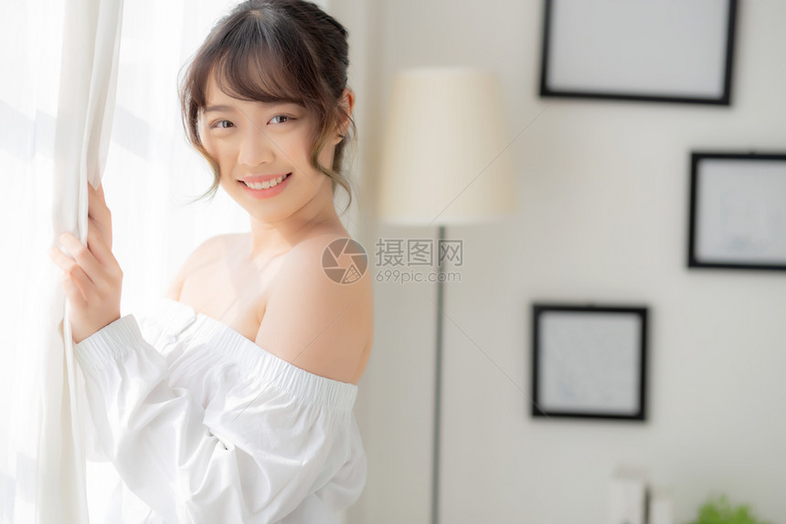 美丽的年轻亚洲女站在窗户边微笑早上醒来时日出女孩对新鲜欢乐生活方式和放松概念感到快乐图片