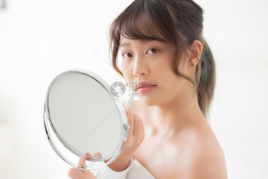 美丽的肖像年轻女看着镜子在房间里涂上化妆口红美唇容的女孩化妆和时尚在家里的口腔生活方式和保健概念图片