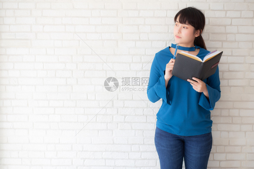 美丽的亚洲女微笑着站立思考写笔记本在混凝土水泥白背景的家庭女孩作业书本教育和生活方式概念图片