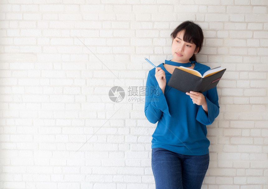 美丽的亚洲女微笑着站立思考写笔记本在混凝土水泥白背景的家庭女孩作业书本教育和生活方式概念图片