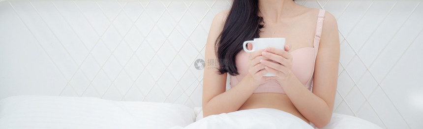 穿着内衣喝咖啡的美丽年轻感女睡在卧室的床上图片
