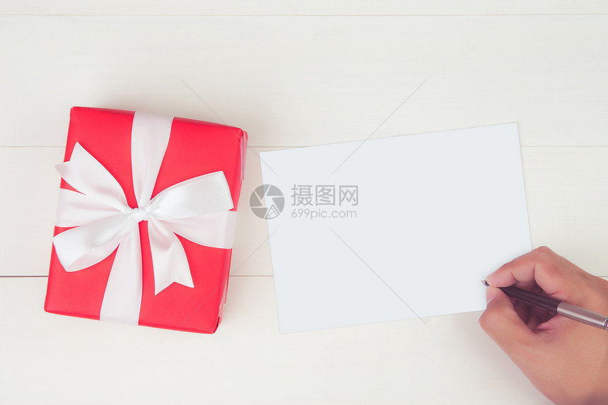 持空白贺卡写信件的人手在木制餐桌上有红色礼品盒现货和包装明信片模型顶视平地复制空间假日概念图片