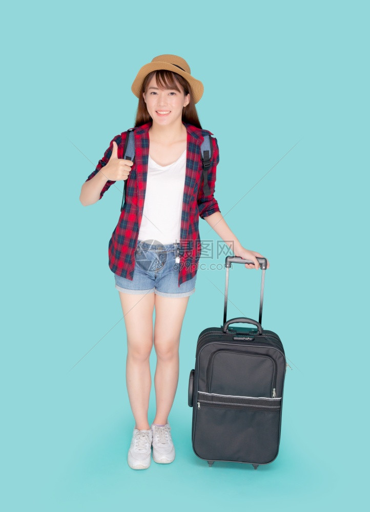 美丽的年轻女士拉着行李箱被蓝色背景孤立asia女孩快乐地拿着行李走和手势拇指在度假时带着兴奋旅行和的概念图片