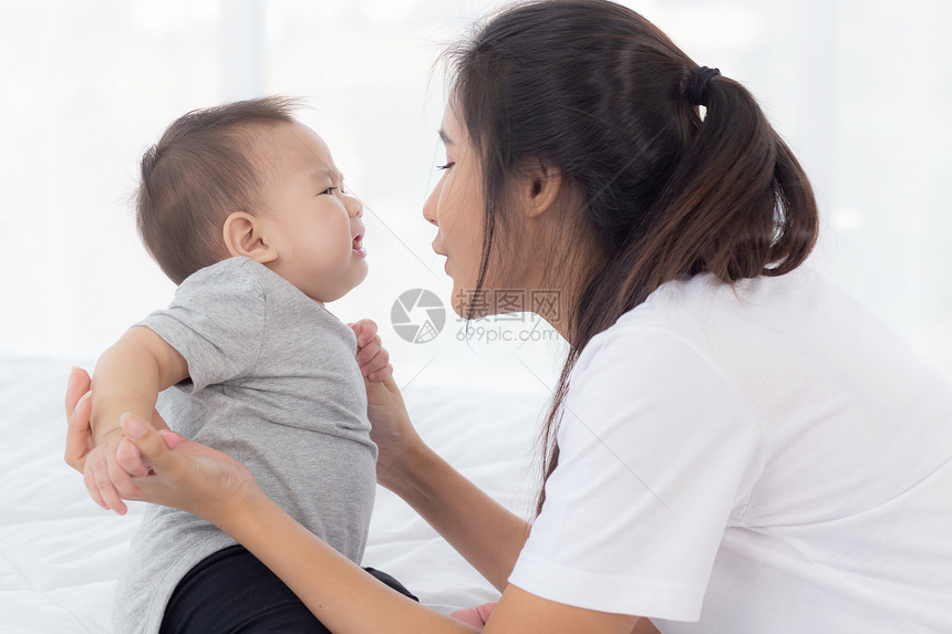 年幼的母亲把小女婴放在家中的卧室里母亲带着孩子和照顾妇女孩子无忧虑幼儿和父母情感表达家庭概念图片