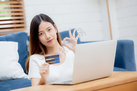 年轻女坐在沙发上使用笔记本电脑在线购物信用卡买到互联网图片